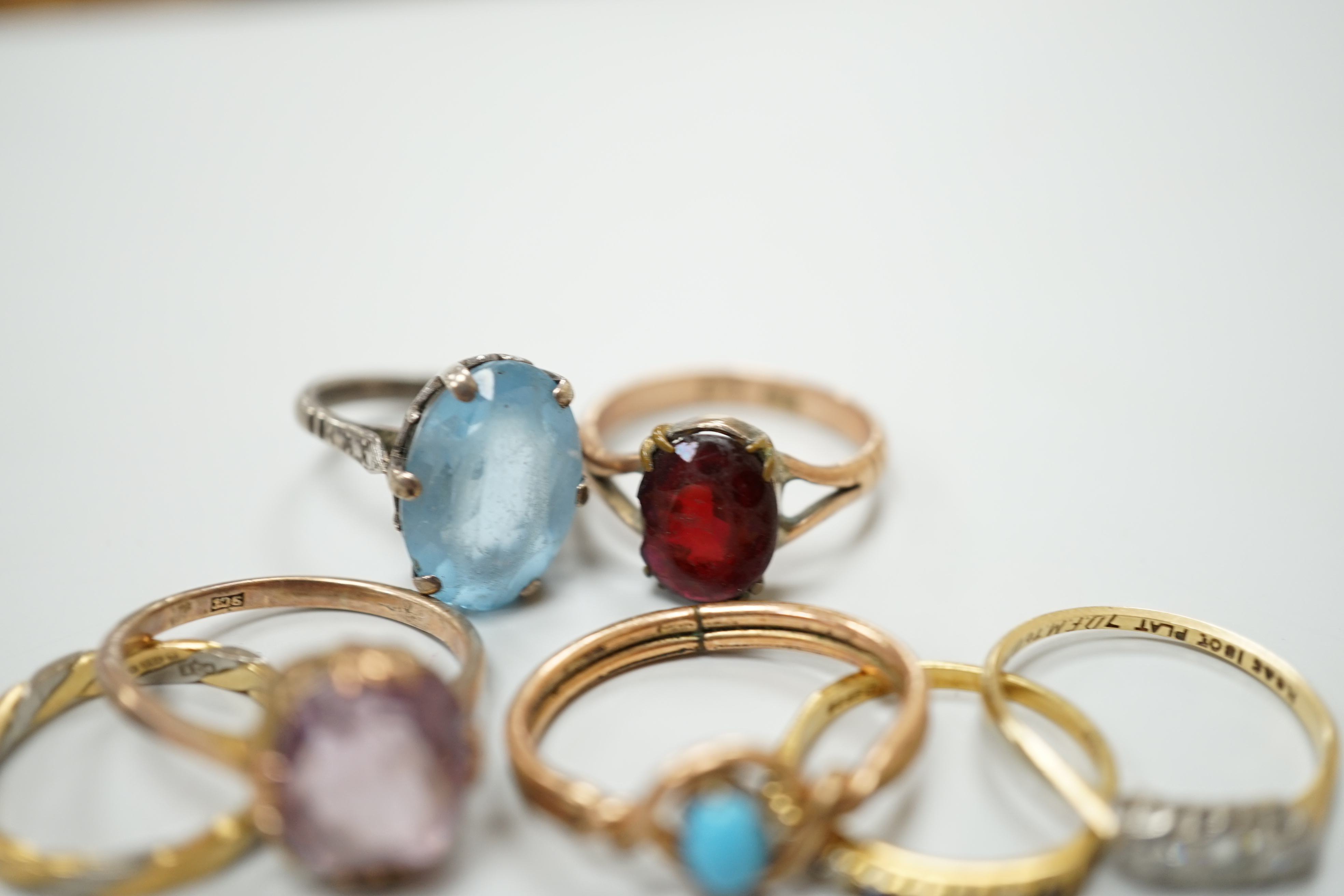 Seven assorted dress rings, comprising an 18ct gold three stone diamond ring, size M, a 9ct gold dress ring with associated worn red stone, size P, a silver ring with blue stone, size I, a 9ct gold and amethyst ring, siz